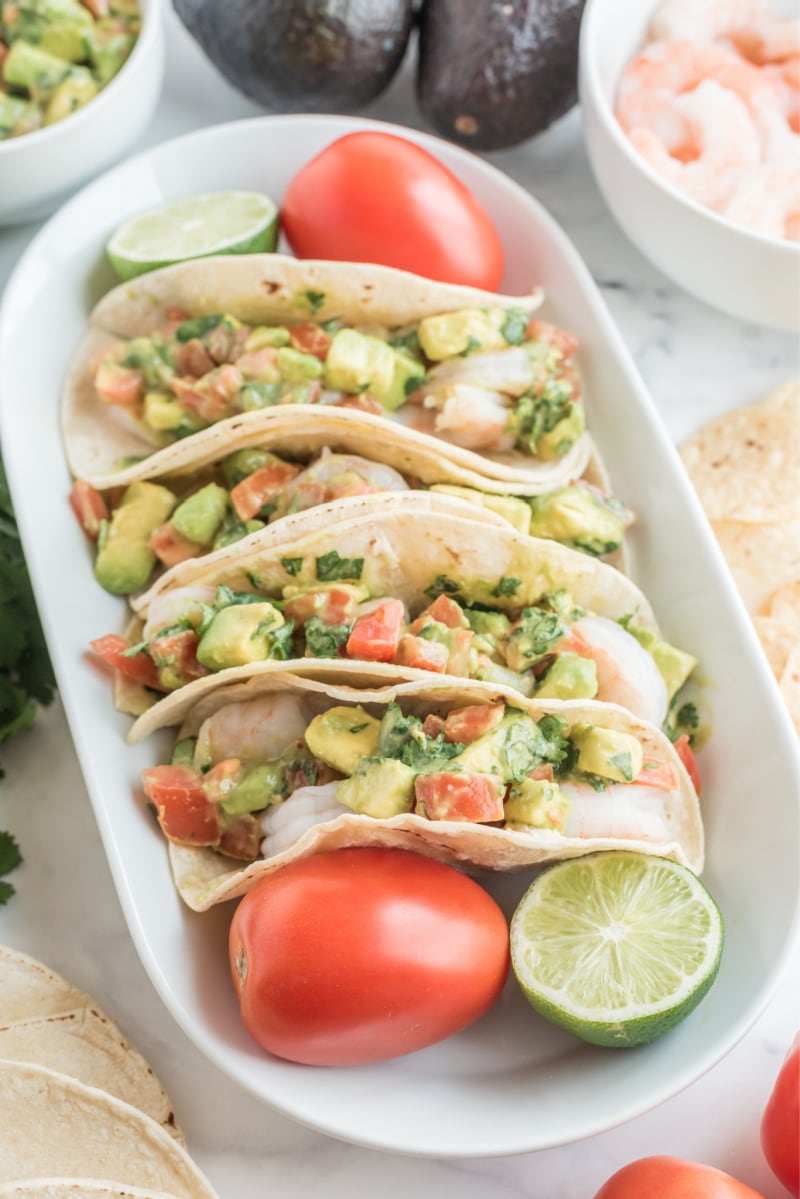 ceviche shrimp tacos displayed on a white platter with tomato and lime