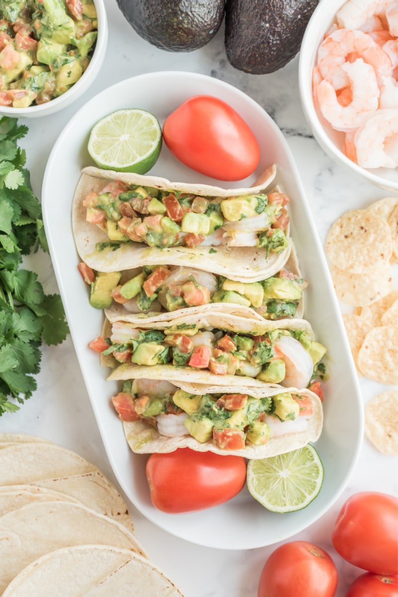 ceviche shrimp tacos displayed on a white platter with tomato and lime