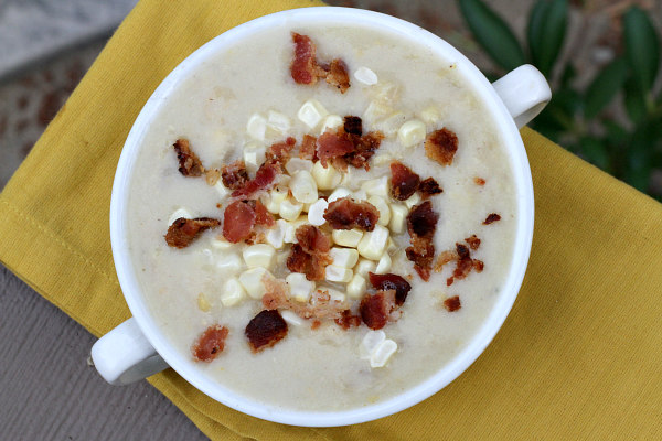 overhead shot of white bowl of fresh corn chowder topped with bacon and set on a yellow napkin