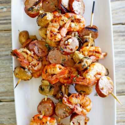 skewers of grilled shrimp sausage and mushrooms on a white platter