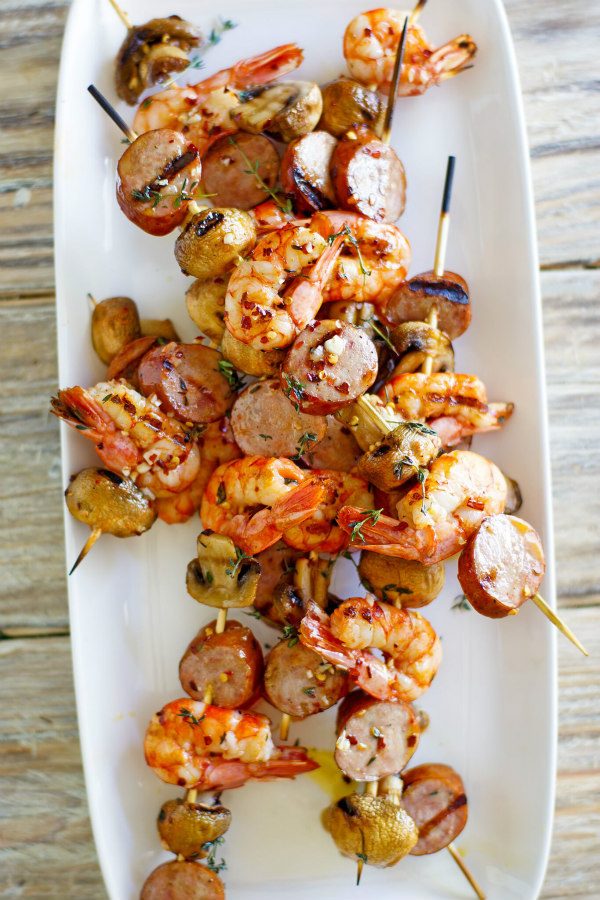 Mixed Grill of Shrimp, Sausage and Mushrooms on skewers displayed on a white platter