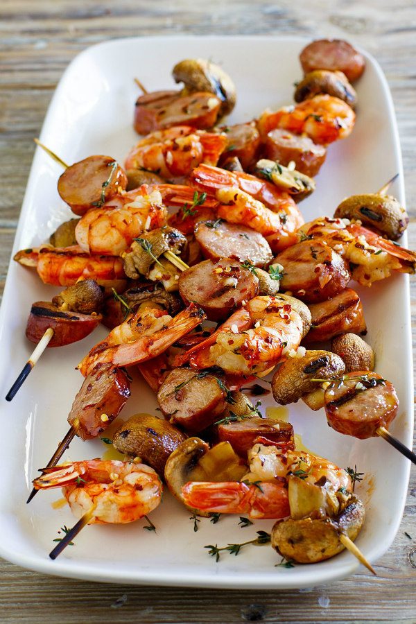 Mixed Grill of Shrimp, Sausage and Mushrooms on skewers displayed on a white platter