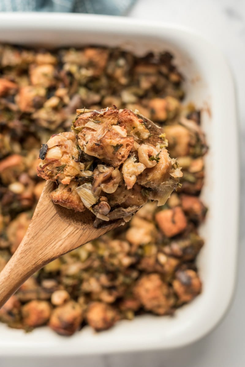 wooden spoon spooning out stuffing out of white casserole dish