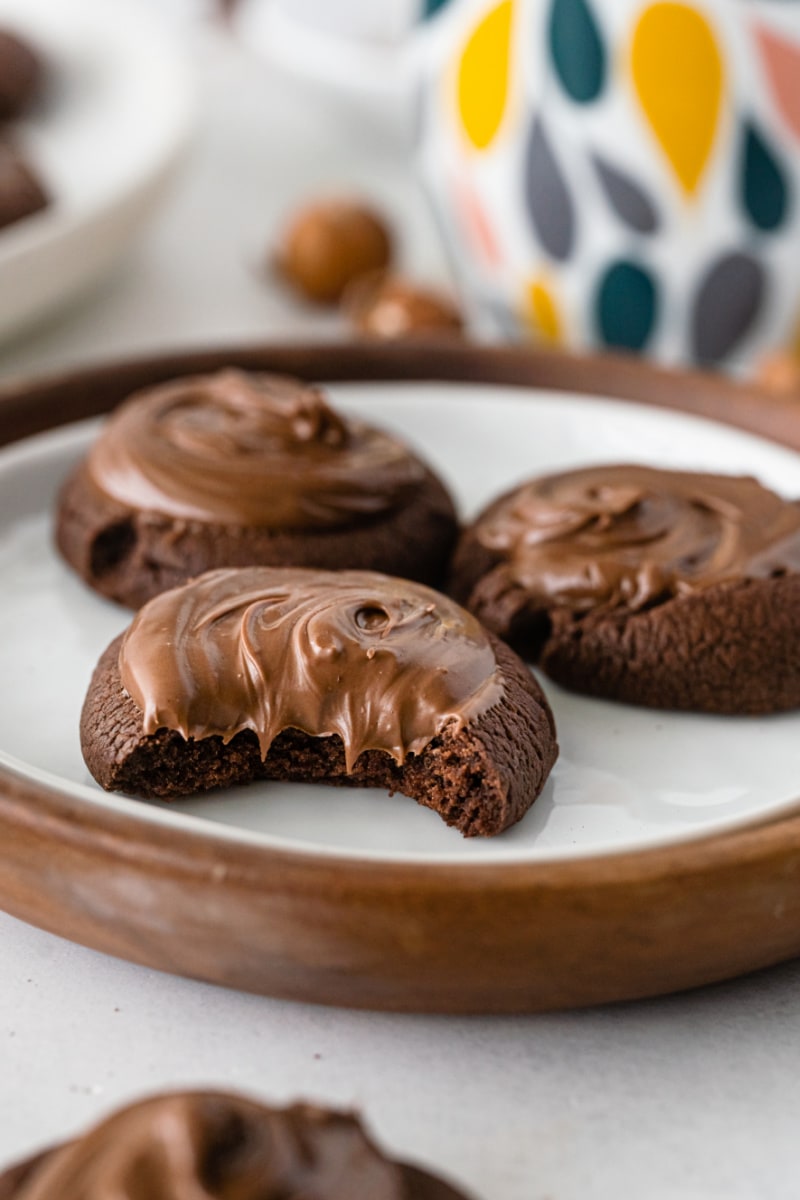 three nutella thumbprint cookies on plate one with bite out of it