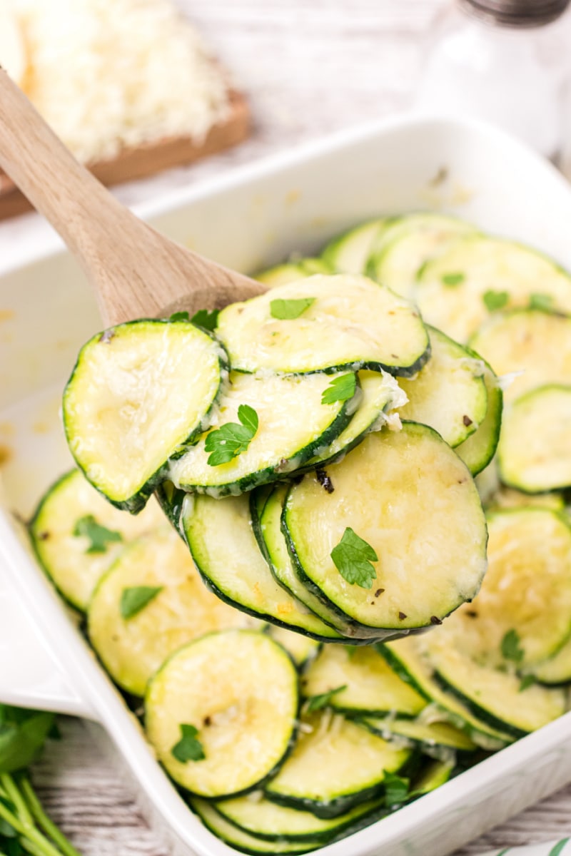 spooning out parmesan zucchini slices out of baking dish