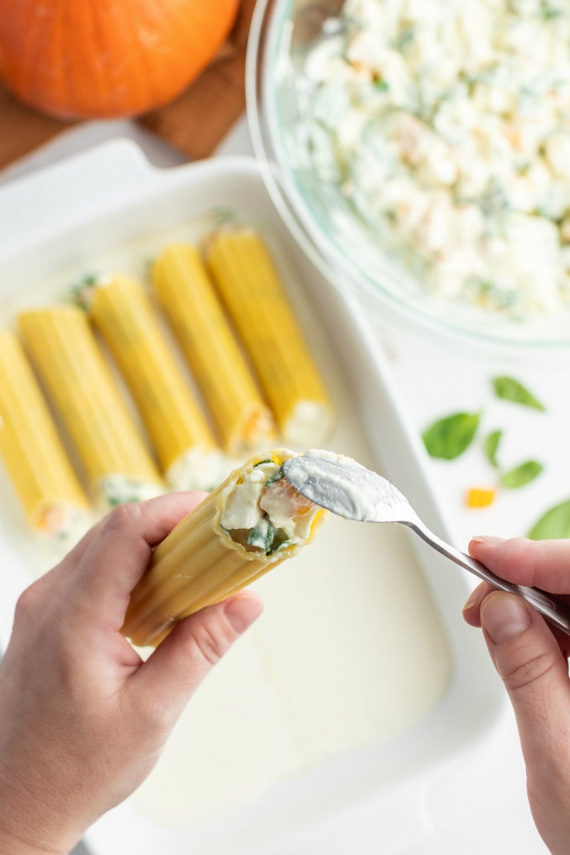 hand showing stuffing manicotti with pumpkin filling