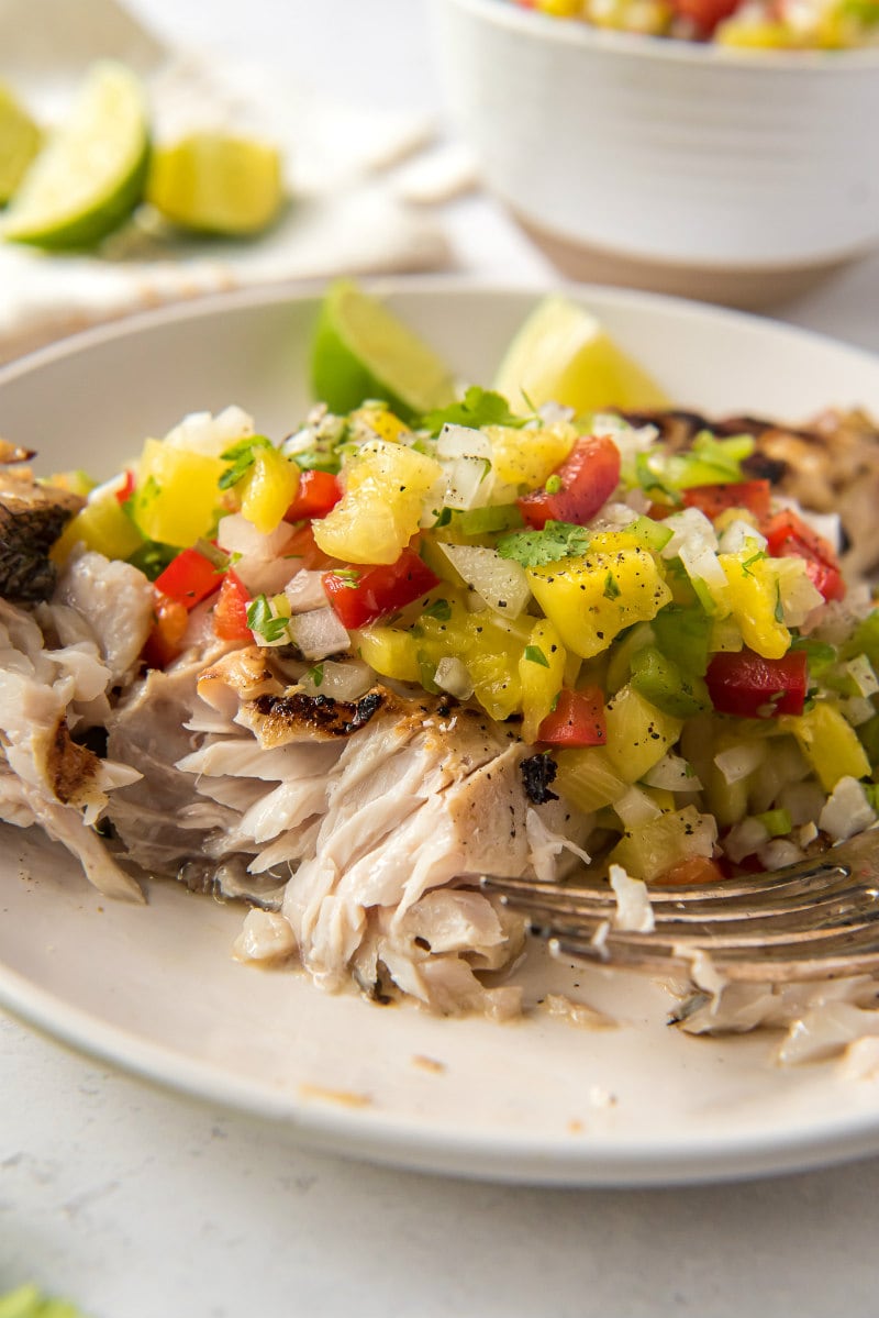 red snapper flaked open with a fork and served with pineapple salsa on a white plate