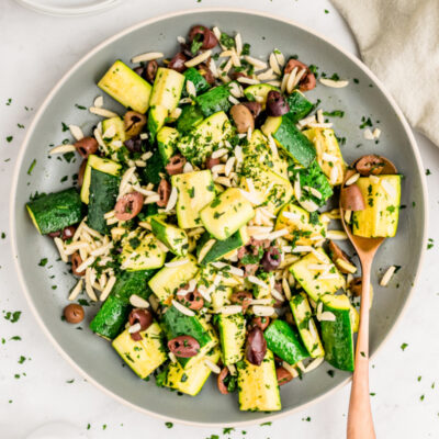 skillet with sauteed zucchini with almonds and olives and a spoon
