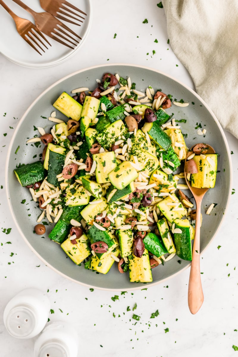 skillet with sauteed zucchini with almonds and olives and a spoon