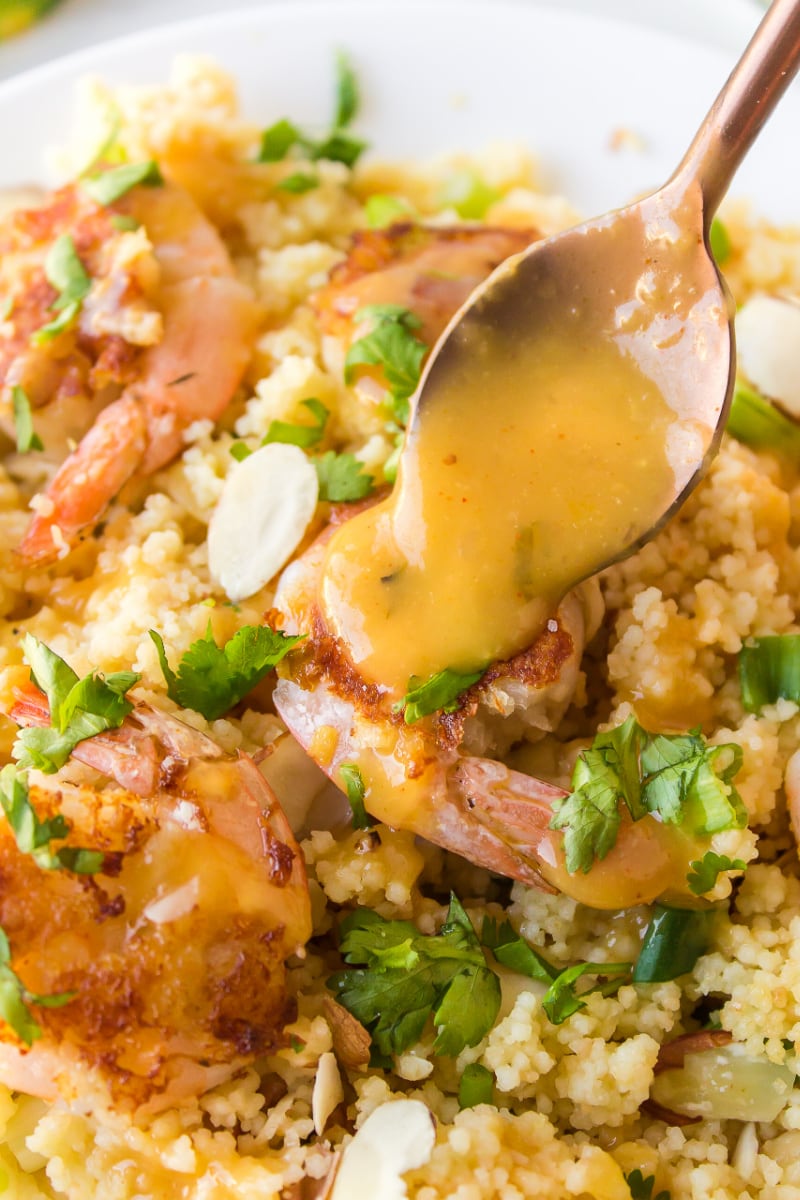 spooning sauce onto shrimp with couscous