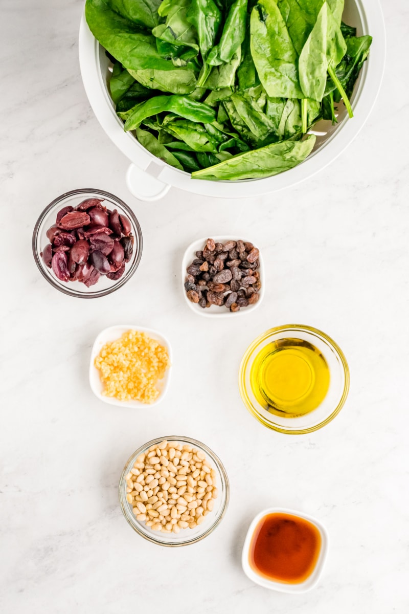 Spinach with Olives, Raisins and Pine Nuts recipe from RecipeGirl.com #spinach #olives #raisins #pinenuts #recipe #RecipeGirl ingredients displayed for making spinach with olives raisins and pine nuts