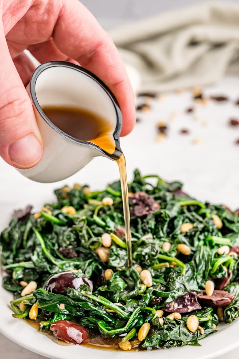 Spinach with Olives, Raisins and Pine Nuts recipe from RecipeGirl.com #spinach #olives #raisins #pinenuts #recipe #RecipeGirl pouring vinaigrette onto sauteed spinach