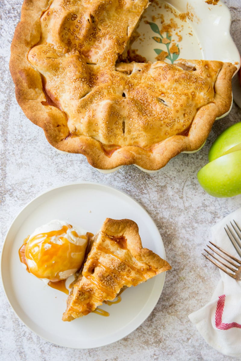 apple pie with slice cut out plated on white plate with ice cream