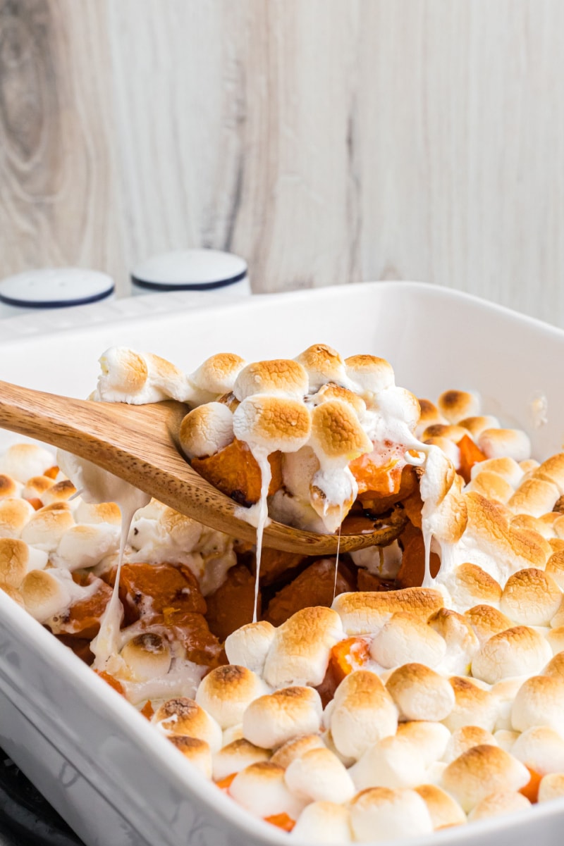 spooning out caramelized yams with marshmallows out of baking dish