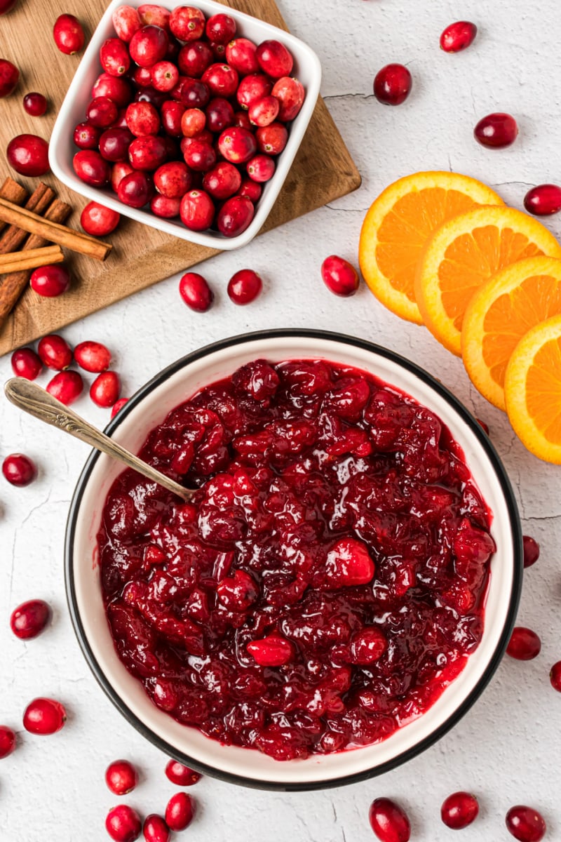 bowl of cinnamon cranberry sauce with fresh cranberries and orange slices in background