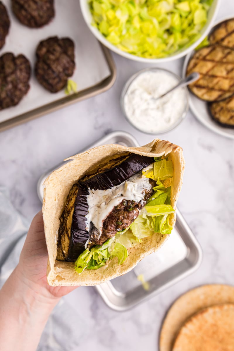 hand holding greek inspired burger in pita