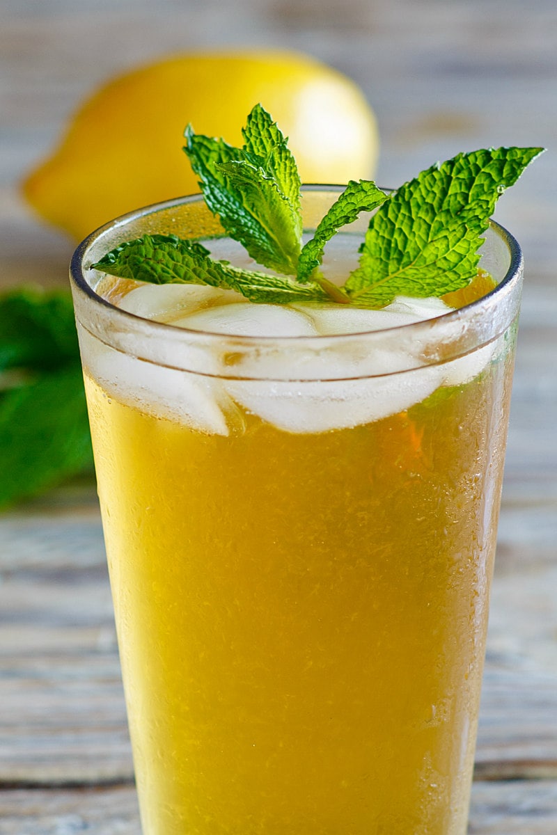 a glass of sweet summer iced tea garnished with fresh mint with a lemon in the background