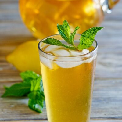 Sweet Summer Iced Tea garnished with mint with a pitcher of iced tea in the background