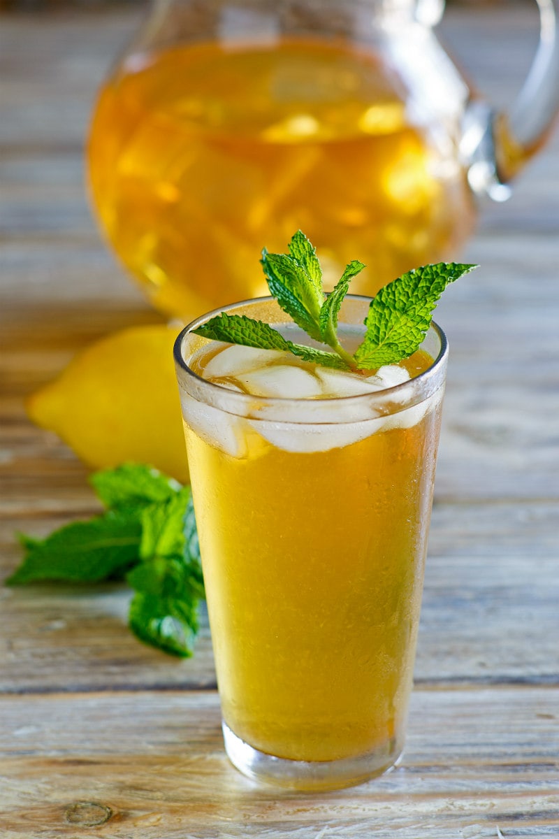 Sweet Summer Iced Tea garnished with mint with a pitcher of iced tea in the background