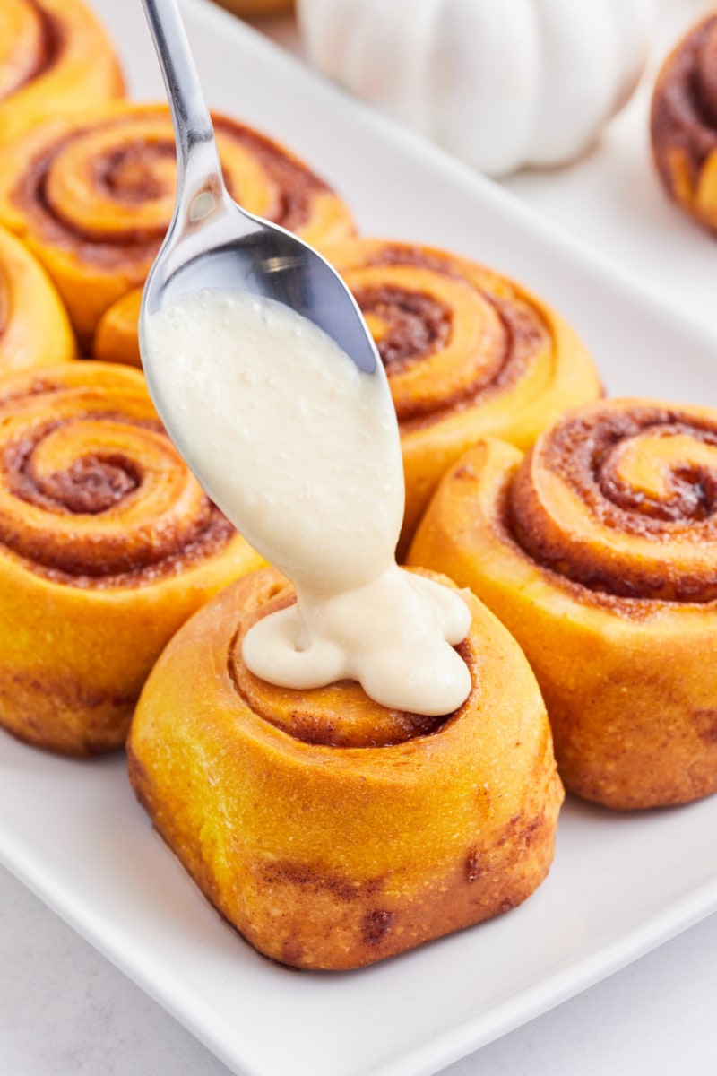 drizzling maple icing onto pumpkin cinnamon rolls