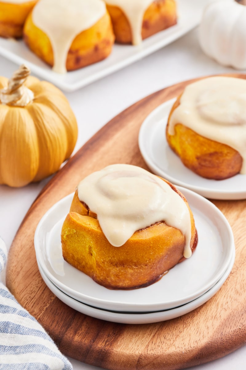 pumpkin cinnamon rolls on white plates with maple icing on top