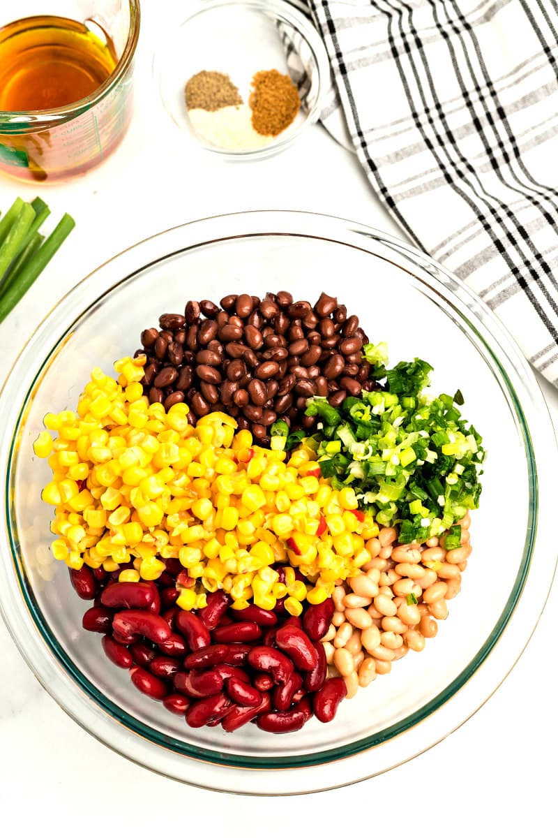 ingredients for red white and black bean salad in a glass bowl with a plaid napkin and green onions garnish