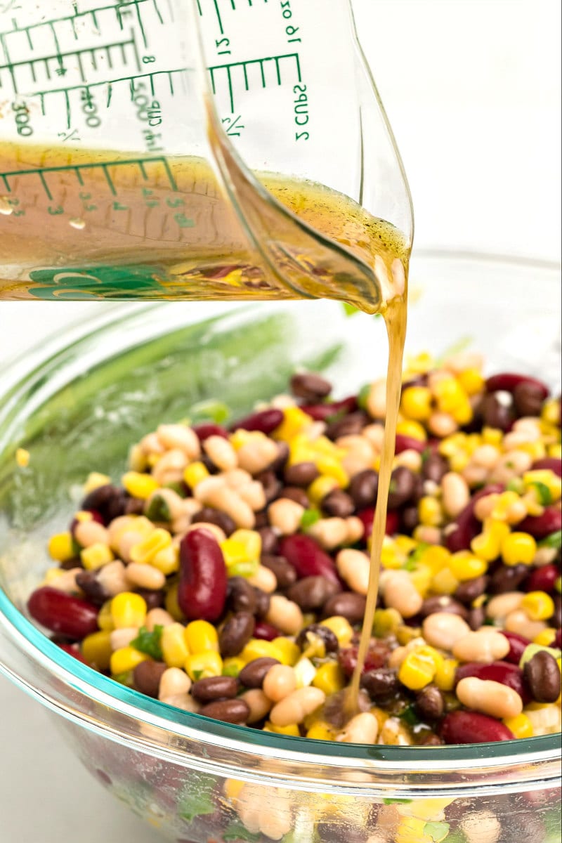 pouring dressing onto red white and black bean salad in a glass bowl