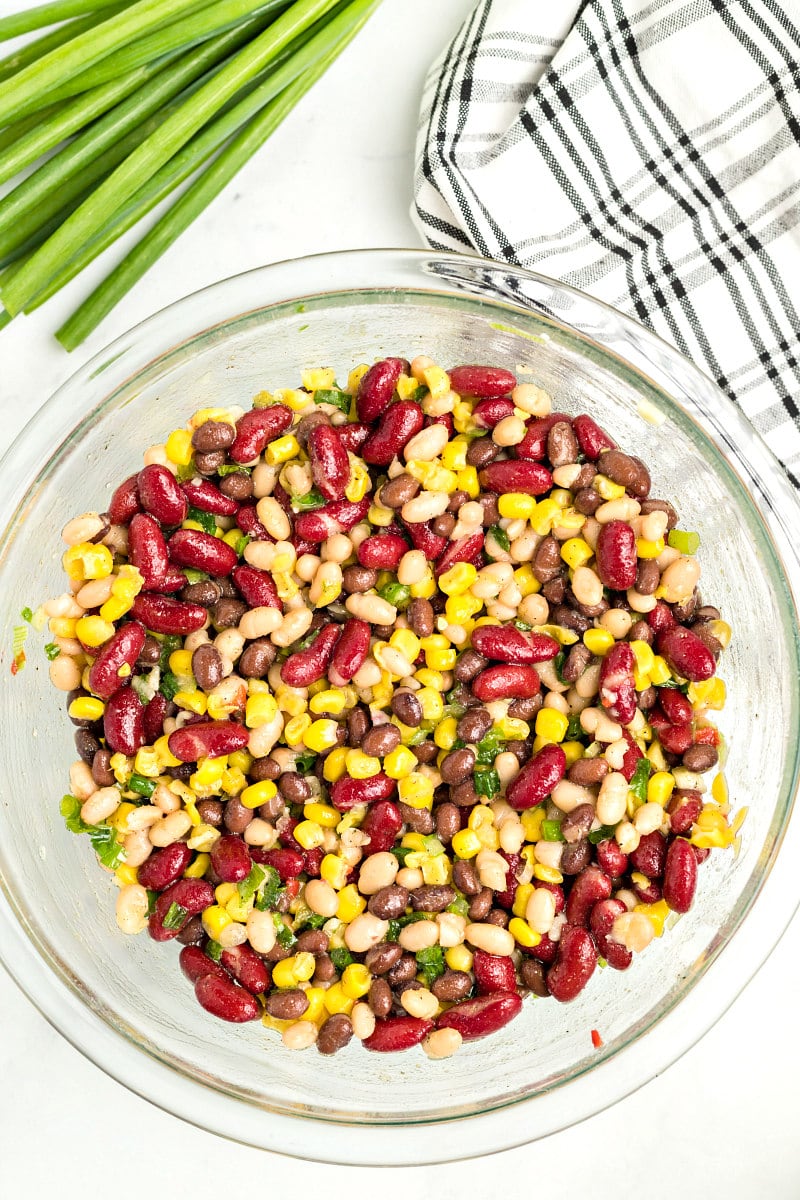 red white and black bean salad in a glass bowl on a plaid napkin with green onions garnish