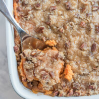 streuseled sweet potatoes in white dish with serving spoon taking some out