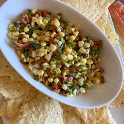 corn and sundried tomato salsa in a white bowl surrounded by tortilla chips