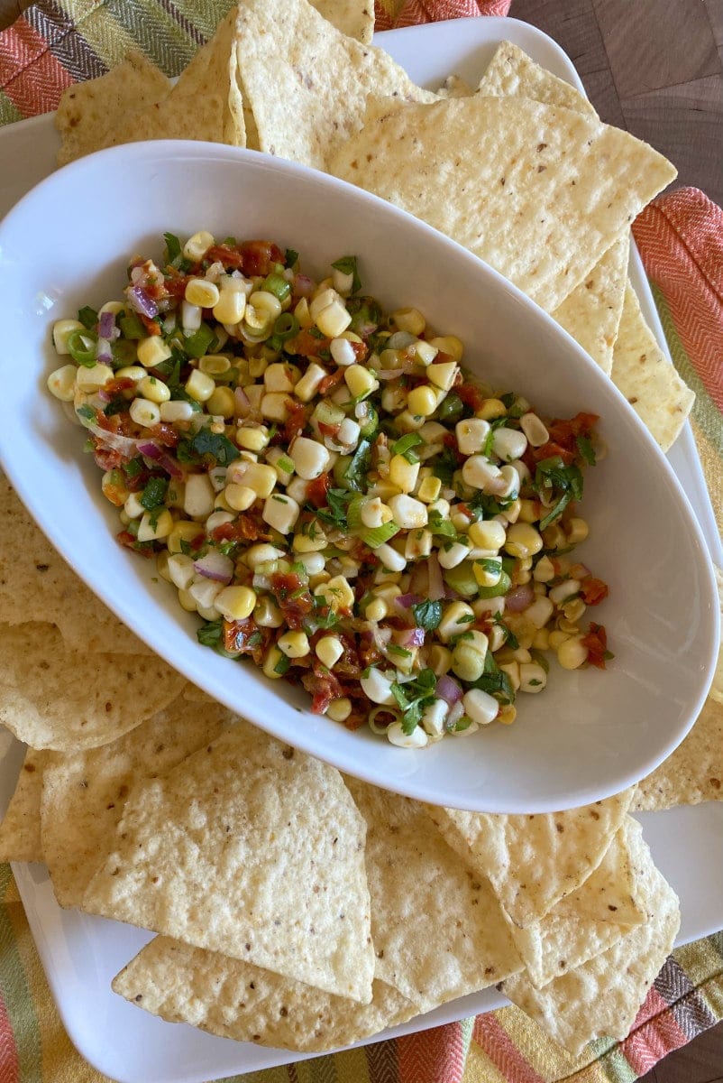 corn and sundried tomato salsa in a white bowl surrounded by tortilla chips