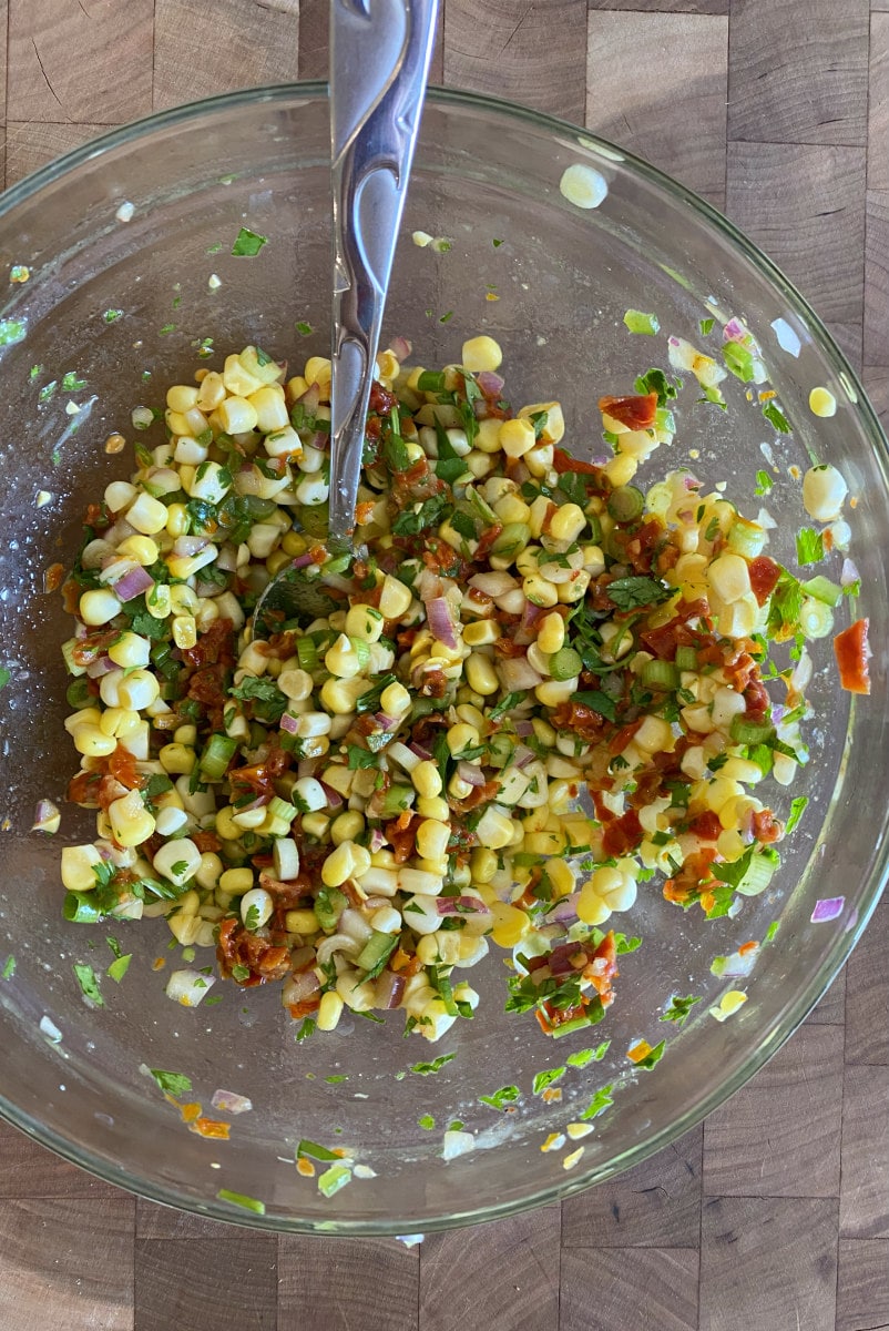 making corn and sundried tomato salsa in a bowl with a spoon