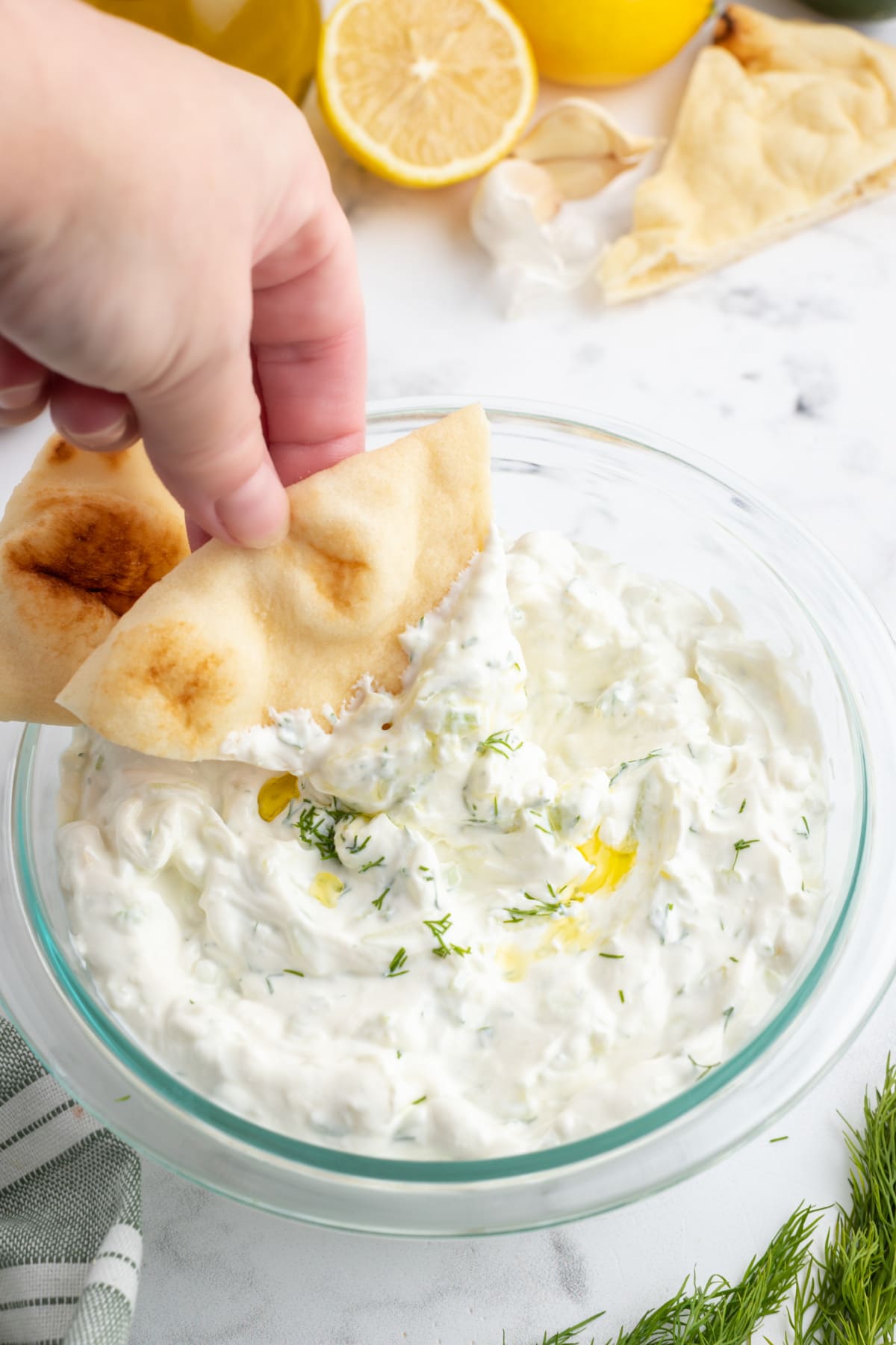 hand dipping pita chip into tzatziki sauce