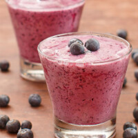 two blueberry lemon smoothies in a glass garnished with fresh blueberries and more fresh blueberries scattered around