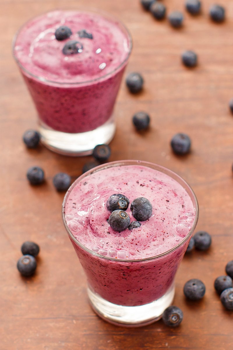 two blueberry lemon smoothies in a glass garnished with fresh blueberries and more fresh blueberries scattered around