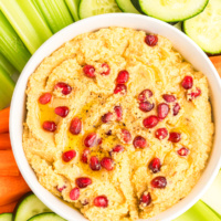 chickpea dip topped with pom seeds and veggies on side