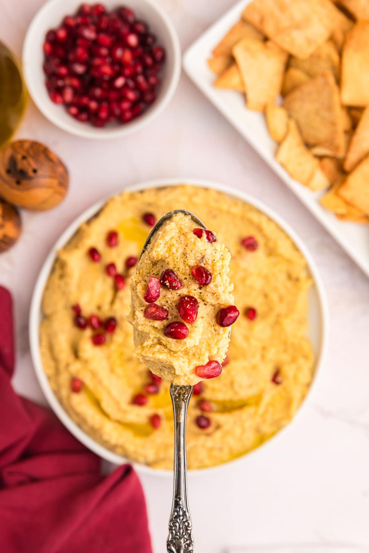 spoonful of chickpea dip over bowl with pom seeds on top