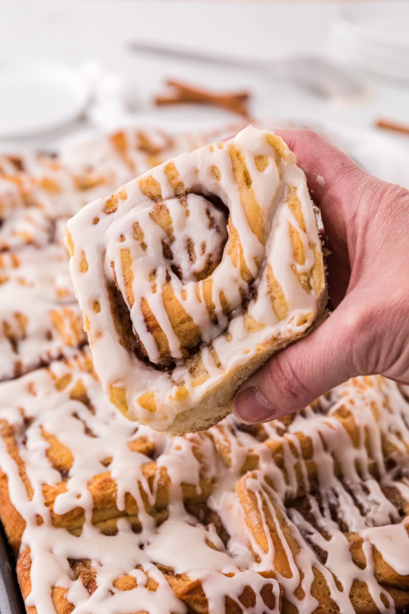 hand pulling cinnamon roll out of pan of cinnamon rolls