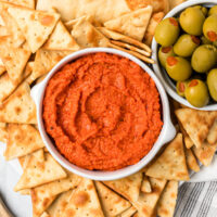 roasted red pepper almond spread in a white bowl with crackers and olives