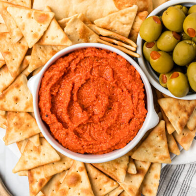 roasted red pepper almond spread in a white bowl with crackers and olives