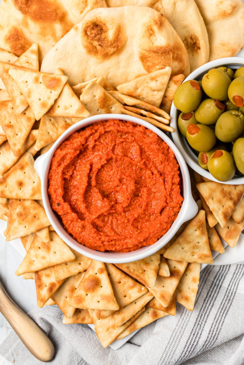 roasted red pepper almond spread in a white bowl with crackers and olives