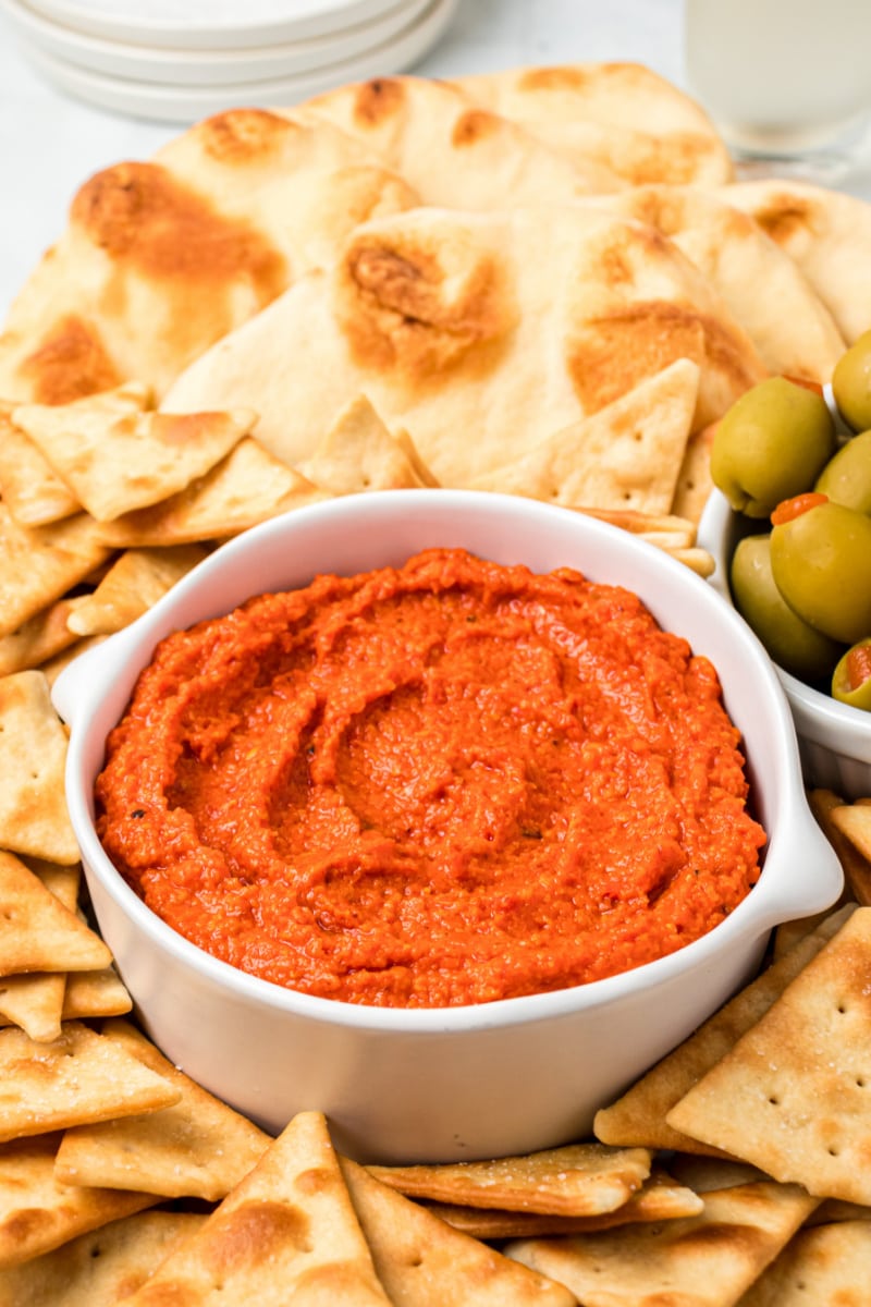 roasted red pepper almond spread in a white dish surrounded by crackers