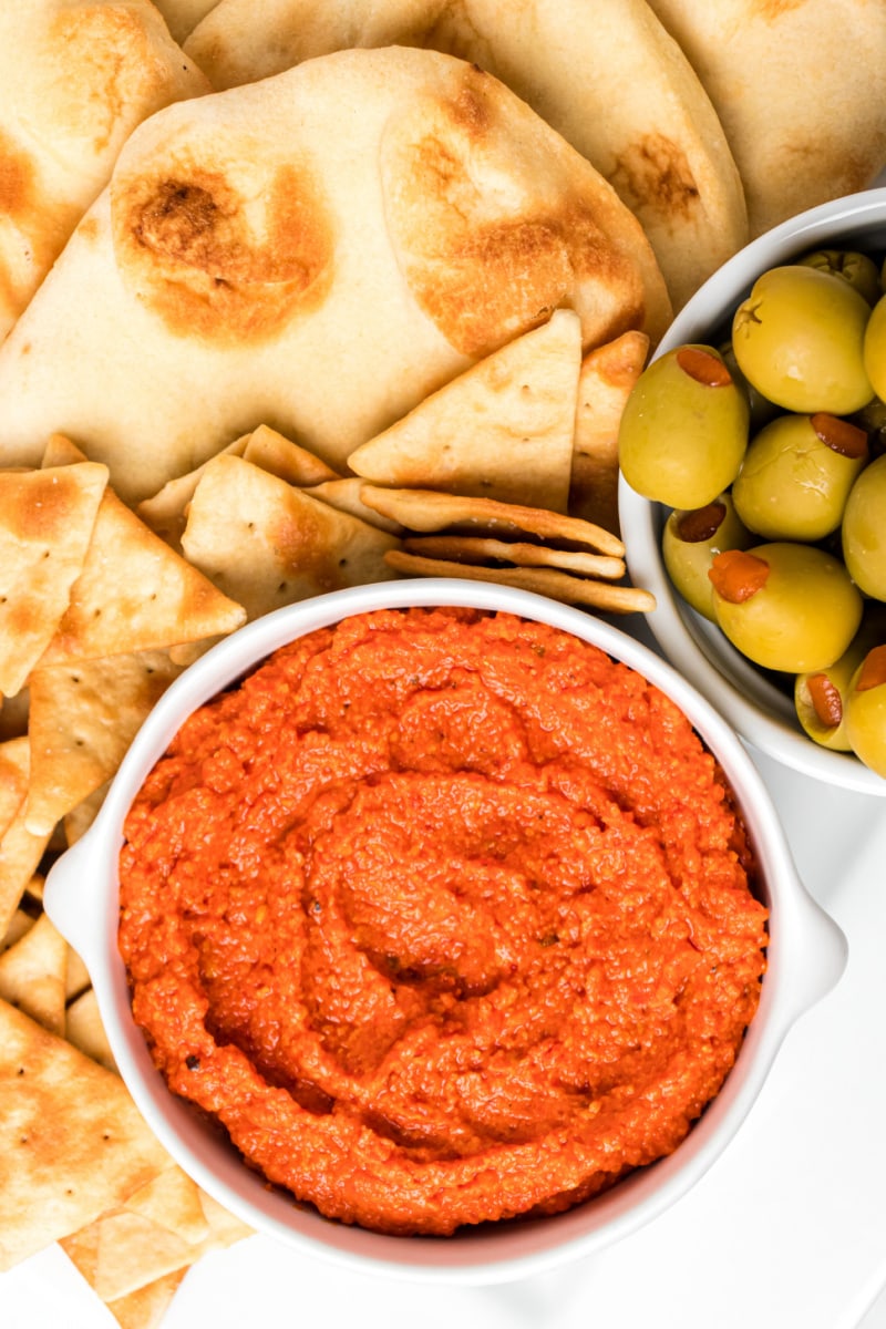 bowl of roasted red pepper almond spread with crackers and olives