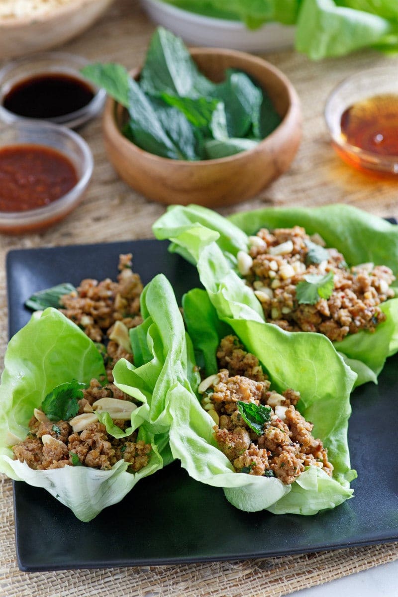 asian lettuce wraps on a black plate with bowls of ingredients in the background