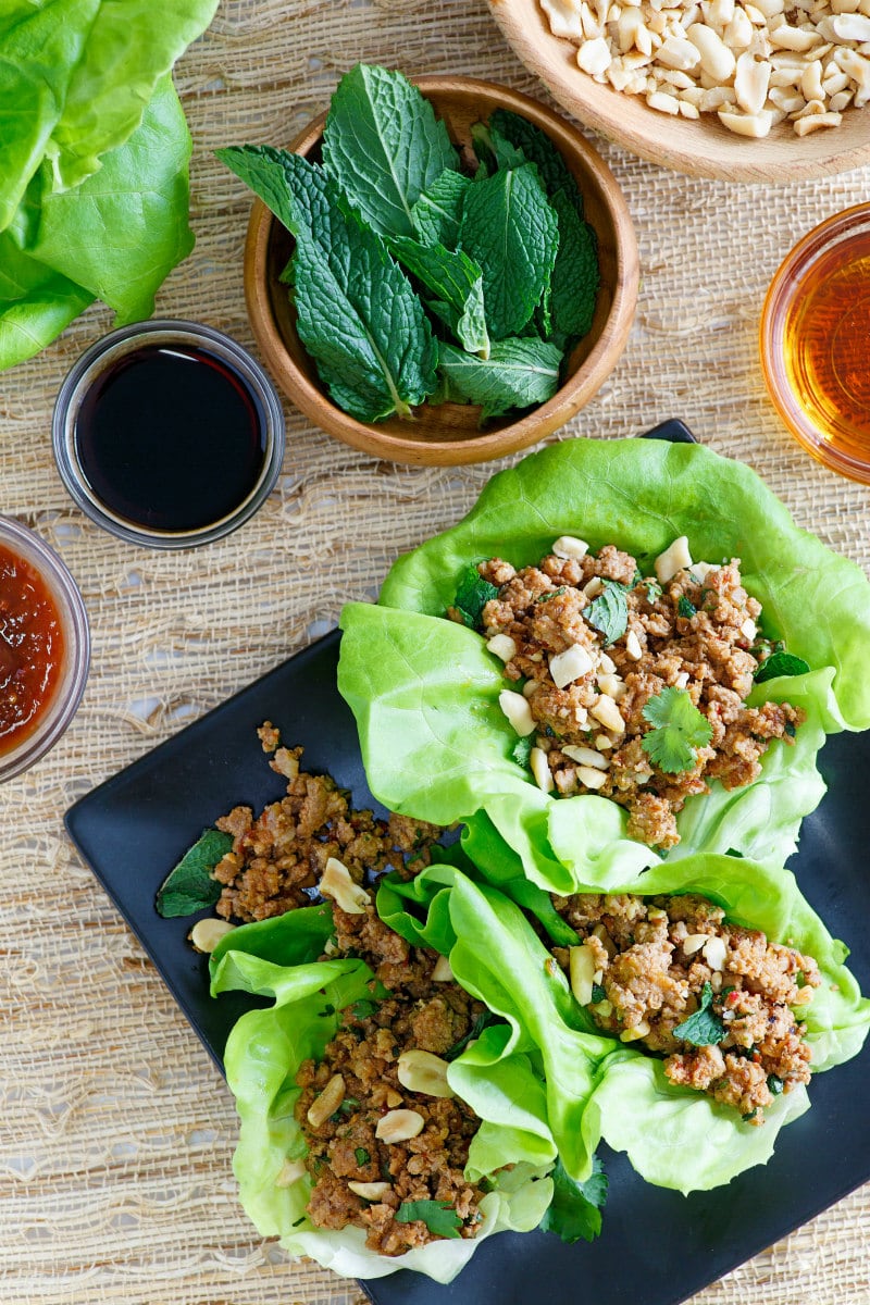 overhead shot of asian lettuce wraps on a black plate with bowls of the prep ingredients displayed