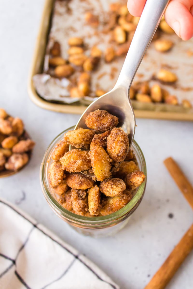 wooden spoon spooning cinnamon almonds into jar