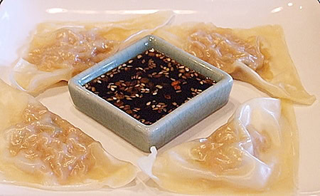 four shrimp dumplings with sesame dipping sauce in the middle