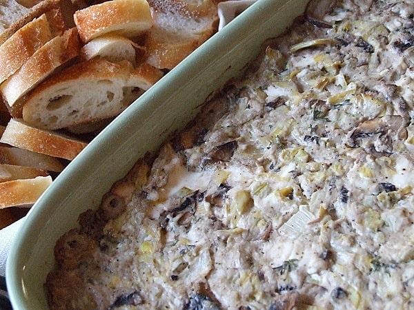 wild mushroom and artichoke dip in a casserole dish with bread slices on the side