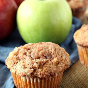 apple cinnamon muffin displayed in front of green and red apples with a blue cloth napkin
