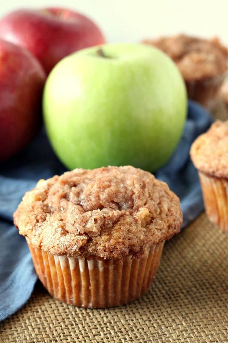 apple cinnamon muffin displayed in front of green and red apples with a blue cloth napkin